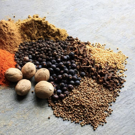 Spices piled on a light grey table: peppercorns, salt, coriander, nutmeg, turmeric & cloves on The Biltong Merchant website