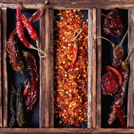 Wooden crate divided into 3 troughs with roasted, dried & raw red chillies & peri peri flakes on The Biltong Merchant website