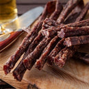 Traditional Fresh Droëwors biltong on wood table with cutting knife & beer, by Simply African Food for The Biltong Merchant